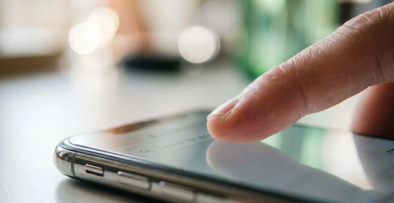 Macro extrême sur un doigt touchant l'écran d'un smartphone avec interface de recherche complètement floutée, faible profondeur de champ, arrière-plan bokeh